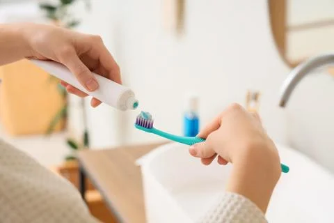 Person applying toothpaste on toothbrush in bathroom Фото