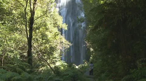 Person approaches the base of a high waterfall Stock Footage 10849779