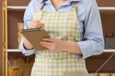 Person in apron writing on notepad in kitchen 스톡 사진
