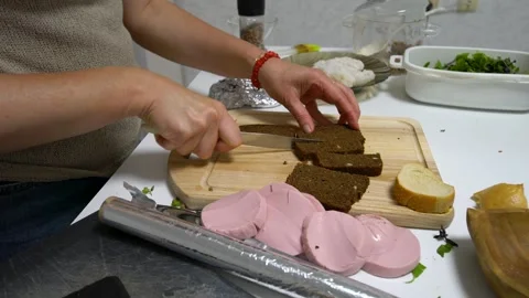 A person is arranging slices of rye bread and pink sausage on aluminum foil, Stock Footage 336064759