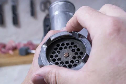 A person assembles a meat grinder-he attaches the grate with a locking disc t Stock Photos