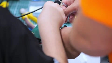 Person assembling electronics with precision tools on a cluttered workbench Stock Footage 346148730