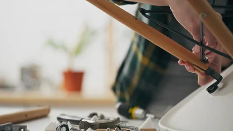 Person assembling furniture with tools on a table surrounded by parts and ma Stock Footage 323712880