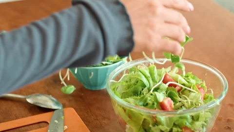 Person assembling leafy green salad with various ingredients in bowl on table 動画素材 271225161