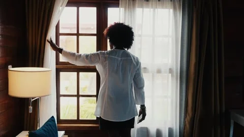 Person from behind white button-down shirt opening sheer white curtains next to Stock Footage 344037033