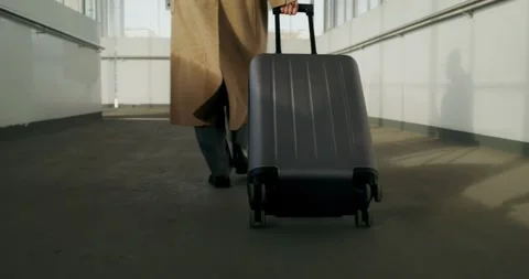 Person in a beige coat pulling a dark gray wheeled suitcase down a hallway. Stock-Footage 297537630