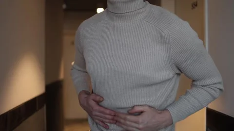 A person in a beige turtleneck bends forward, pressing their hands against their Stock Footage 291550453