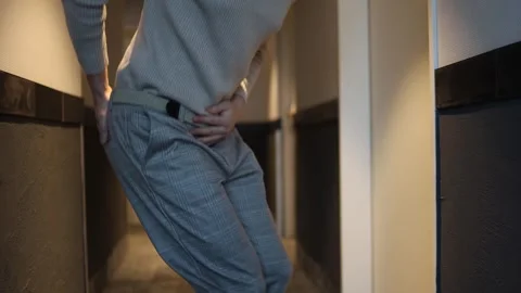 A person bends forward in a hallway, holding their lower abdomen, indicating an  Stock Footage 291551028