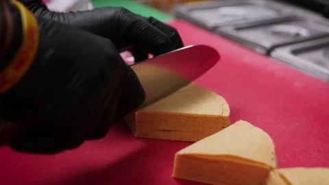 Person in black gloves slicing a stack of food dough on a red surface. Stock Footage 331634610