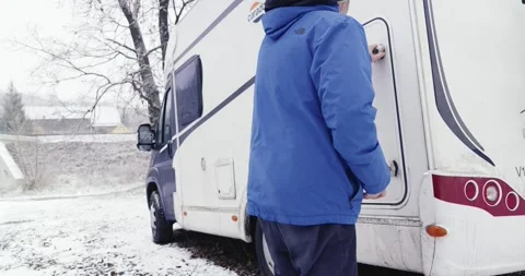 A person in a blue jacket opens the back door of a white caravan parked on Stock Footage 257673707