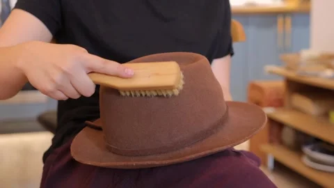 Person brushing brown felt hat indoors Stockbeeldmateriaal 337946468