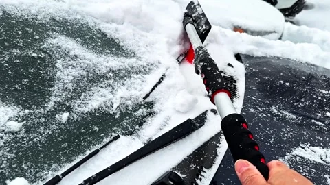Person brushing snow off car windshield Stockbeeldmateriaal 331403124