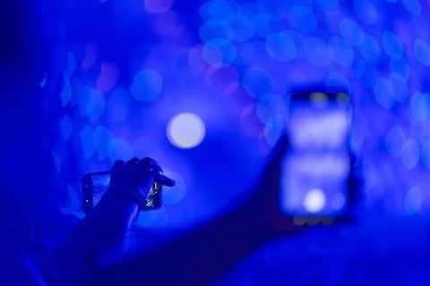 Person capturing vibrant blue bokeh lights with smartphone at night event sce Stock Photos