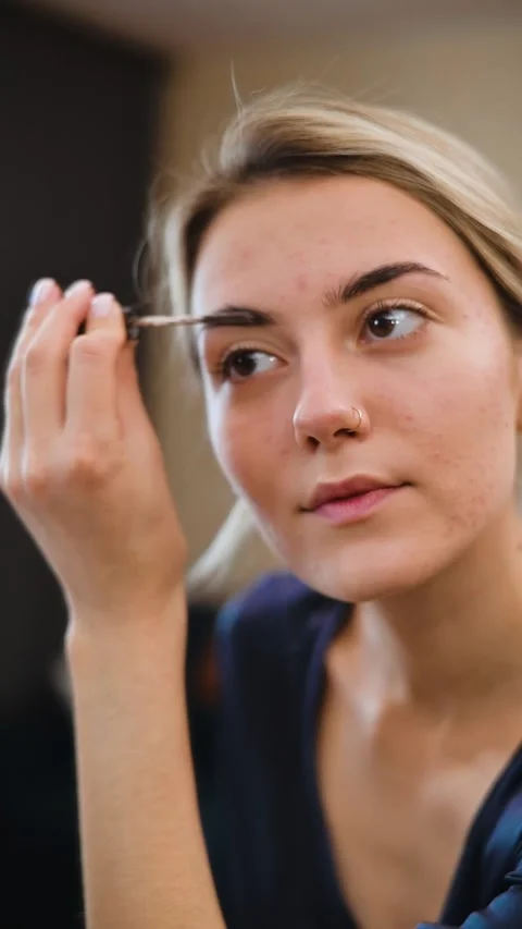 A person is carefully applying makeup to their eyebrows, showcasing a daily Stock Footage 337555530