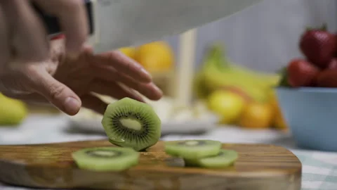Person carefully cutting kiwi with sharp knife on cutting board - closeup Stock Footage 341228666