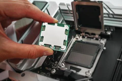 A person is carefully holding a computer processor above a motherboard socket Stock Photos