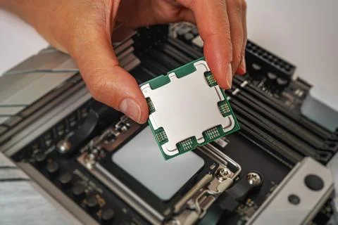 A person is carefully holding a computer processor above a motherboard socket Foto stock