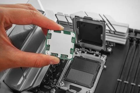 A person is carefully holding a computer processor above a motherboard socket Foto stock
