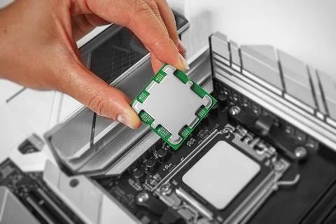 A person is carefully holding a computer processor above a motherboard socket Stock Photos
