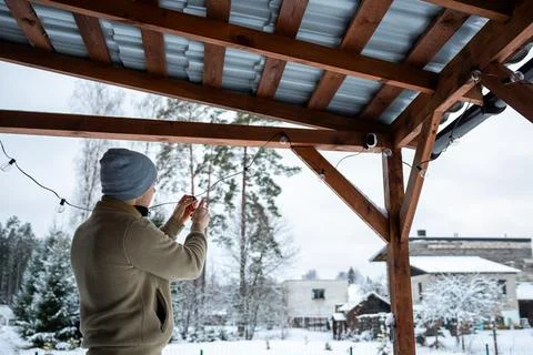 Person Changing LED String Lights on Terrace in Snowy Residential Area Stock Photos