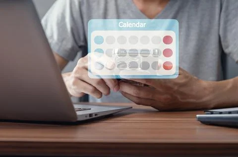 Person Checking Calendar Icon on Mobile Device Near Laptop Stock Photos