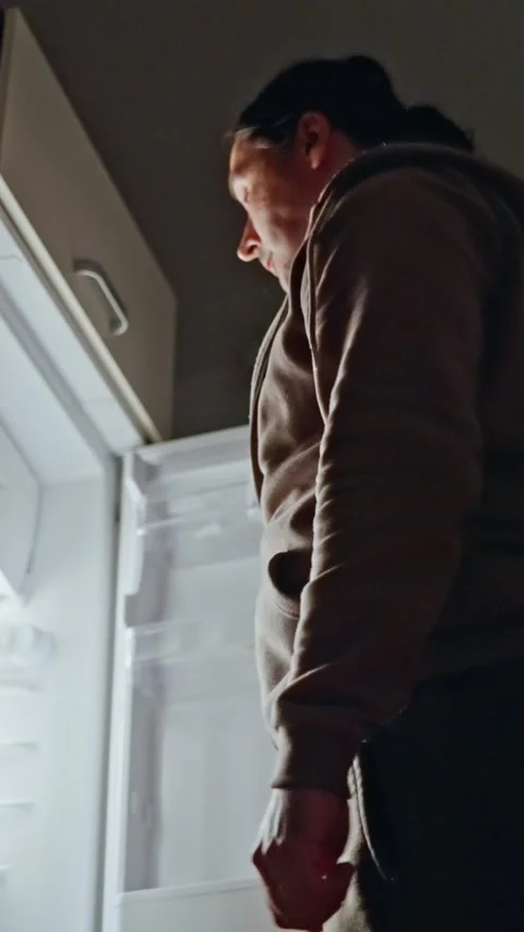 A person is checking an empty refrigerator late at night, contemplating cooking Video stock 312477813