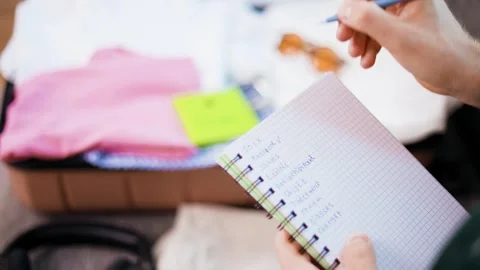 Person checking off items on a travel packing list in notebook during vacation p Stock Footage 343752731