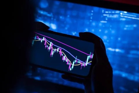 Person checking a stock chart on a phone in front of a glowing screen Stock Photos
