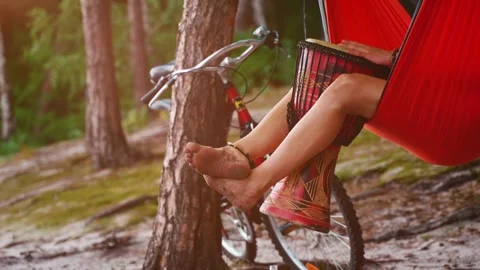 Person chilling in hammock in forest and play reggae on small African hand drum Stock Footage 339767103
