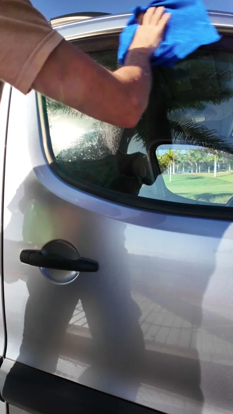 Person cleaning a silver car window with a spray bottle and blue cloth Video stock 332020796