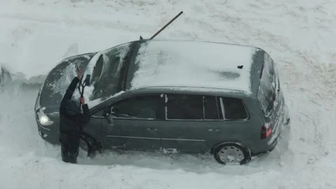 Person cleaning snow from windshield of car buried in deep snowdrift during Stock Footage 344846892