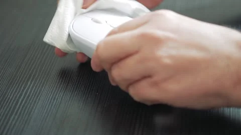Person cleaning white computer mouse with tissue on dark wood surface Stockbeeldmateriaal 347148280