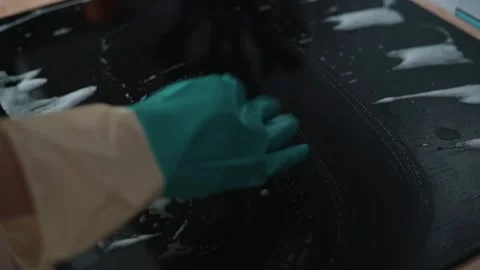 A person cleans a black surface using a sponge and soap. Видео 337112170