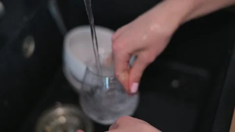 A person cleans glassware under running water, demonstrating proper washing 動画素材 337642784