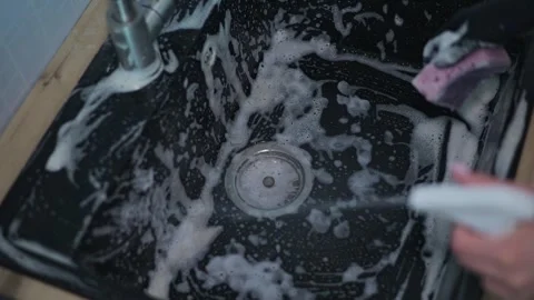 A person cleans a sink using soap and water, scrubbing away dirt and grime. This 库存影片 337642854