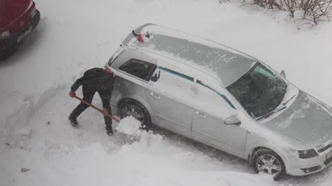 Person clearing deep snow from around silver station wagon car caught in severe Stock Footage 344865037