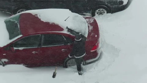 Person clearing deep snow from red sedan after heavy snowfall during harsh Stock Footage 326752187