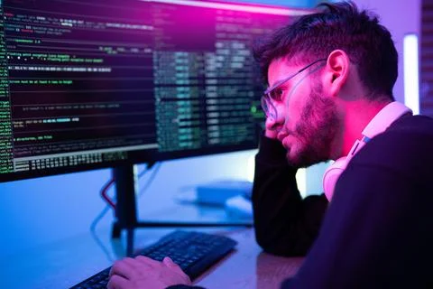 Person coding at night in a dimly lit workspace with colorful lighting and .. Stock-Fotos