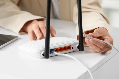 Person connecting an ethernet cable to a white wireless router on a desk, int Stock Photos
