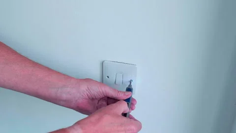 Person connects device to wall outlet and removes front retaining screws. Stock Footage 340615763