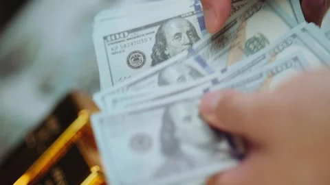 Person counting stack of hundred dollar bills with gold bars on the table. Stock Footage 337599112