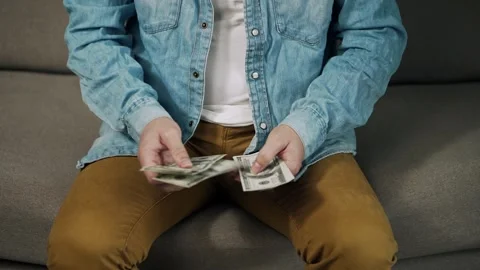 Person Counting Stack of US Dollar Banknotes While Sitting on Sofa Stock Footage 340857210
