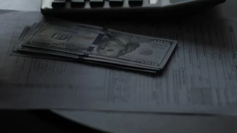 A person counts a stack of hundred-dollar bills using a calculator next to .. Stock Footage 348276321