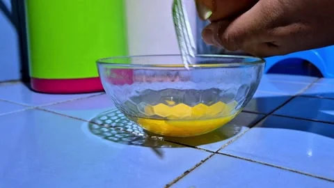 A person cracking and pouring a raw egg into a clear glass bowl Stock Footage 337427557