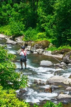 Person crossing river on cable while wearing safety harness. Georgia Stock Photos