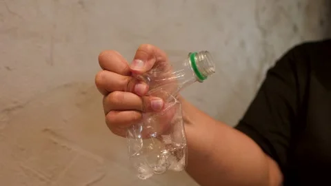 Person Crushing Clear Plastic Bottle for Recycling and Waste Reduction Stock Footage 345099849