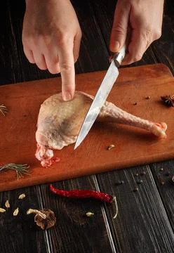 A person cuts a chicken leg with a sharp knife on a wooden cutting board. Dif Stock Photos