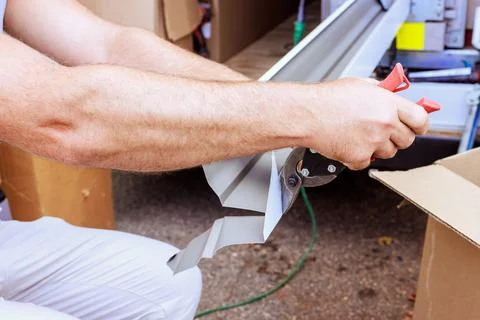 Person cuts gutter metal while sitting near cardboard boxes during renovati.. Stock Photos
