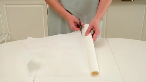 Person cuts a roll of baking parchment paper with scissors on a kitchen table, Stock Footage 309879793