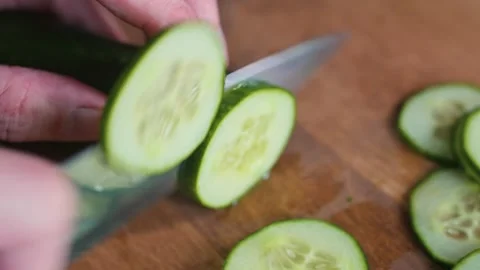 A person is cutting cucumber into thin slices on a wooden cutting board with a Stock Footage 338290246